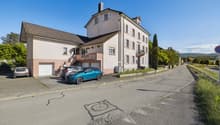 2-story house, tan and pink exterior, brown roof, large windows, 2 cars parked in garage, driveway