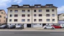 4 story apartment building, beige exterior, multiple windows, garage, multiple cars parked in front