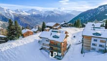 Snow-covered mountain village with wooden chalets, apartment buildings, and scenic mountain views in the background
