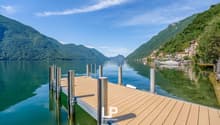Scenic view of a lake surrounded by mountains, with a wooden dock in the foreground and buildings on the shore in the distance.
