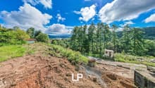 Excavations site, sloped land, grassy areas, trees, distant mountain views, lake in the distance, pathway, utility pole