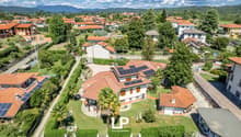 Multiple houses, solar panels on roofs, driveway, garden, greenery, trees, distant mountains, aerial view