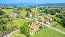Detached house, red roofs, green landscape, visible solar panels, large green fields, mountain view in the distance, swimming pool on the side