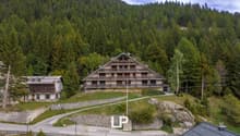 Large apartment building, nestled in a mountainous setting, surrounded by trees, with a scenic mountain backdrop