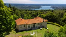 House with terracotta roof, set on a hillside, surrounded by greenery, overlooking a valley and a lake.