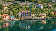 Terraced houses with various architectural designs and colors, under construction buildings, a crane, surrounded by trees and mountains, reflecting on the calm lake