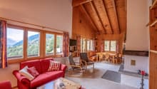 wooden walls and ceiling, fireplace, large windows with mountain views, red sofa, wooden coffee table, dining table and chairs