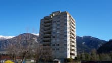 High-rise building with multiple floors and balconies, surrounded by trees and mountains