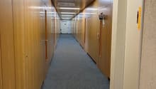 long hallway with wooden lockers on both sides, gray carpet flooring, white ceilings with LED lighting, door at the end