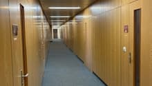 Long hallway with wooden paneled walls, fluorescent lighting fixtures, and a carpeted floor.