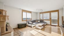 Vom Korridor aus öffnet sich der Blick in das warme, grosszügige Wohnzimmer, das mit seinem direkten Zugang zum Balkon eine angenehme Verbindung nach draussen schafft