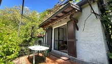 small single-family house, white wall, wooden balcony, brown shutters, open door, small garden table