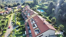 Multi-story apartment buildings with red tile roofs, surrounded by lush greenery and a swimming pool in the center of the complex