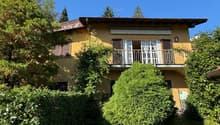 2-story yellow house with a balcony, surrounded by lush greenery and trees