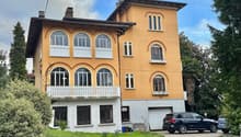 3-story yellow house with arched windows, decorative trim, and a balcony. The house has a garage and is surrounded by trees and greenery.