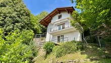 modern design two-story house, white exterior, wooden balcony, lush greenery around