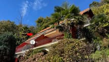 Red and white house, large balcony, red roof, balcony railing, surrounded by greenery and trees