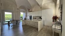 white modern kitchen with marble countertop, central island with sink, dining table with chairs, window with view to garden