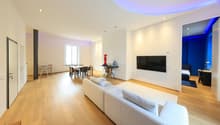 large living room with sofa, coffee table, dining area with table and chairs, flat screen TV, large window, wood flooring