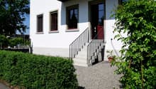 white house, red door, concrete steps, gravel driveway, hedges, trees
