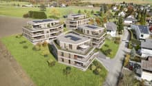 Multiple residential buildings, solar panels on roofs, landscaped gardens, wide open fields, surrounding trees, driveway