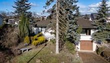 Detached house, gable roof, white walls, brown roof, wooden garage, trees, bushes, bench