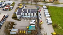 Aerial view of a parking lot with multiple vehicles parked, a building with solar panels, and a road with cars.