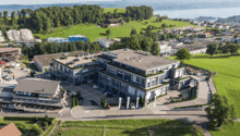 4 story building, surrounded by parking lot, several parked cars, landscaped gardens, hilly green surroundings