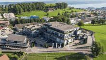 4 story building, surrounded by parking lot, several parked cars, landscaped gardens, hilly green surroundings