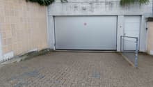A concrete garage with two doors, one large and one small, and a small paved area in front.