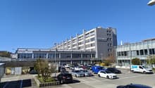 Large office building with multiple floors, surrounded by a parking lot with many cars parked.