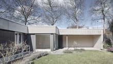 House exterior with two floors, large windows, well-manicured garden, concrete structure, trees in the background.
