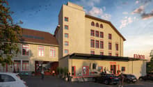 3-story building with arched windows, red trims, entrance with large canopy, sign reading FLOOS MAGAZINE, multiple parked cars