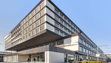 A modern, multi-story office building with a sleek, angular design. The building has a large, prominent sign that reads 'Ambassador House' on the front facade. The exterior is composed of a mix of glass, metal, and concrete materials, creating a contempor