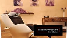 The image shows a relaxing spa or massage room with a comfortable reclining chair, wooden furniture, and decorative elements like framed artwork and vases with flowers. The room has a warm, calming atmosphere with a fireplace and what appears to be a balc