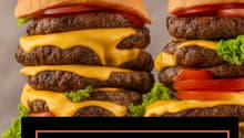 Two hamburgers stacked on top of each other, with multiple layers of beef patties, cheese, lettuce, and tomato.