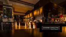 modern bar with wooden counters, yellow lighting, shelves with bottles, chalkboard menu, plant