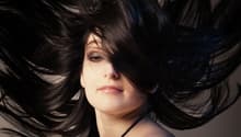 Woman with long black hair, wearing a black dress, looking at the camera, with a blurry background