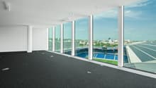 Large open office space with floor-to-ceiling windows overlooking a sports stadium and city skyline. The space has a black tile floor and white walls. There are several lighting fixtures installed in the ceiling.