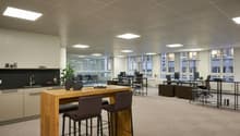 Large open-plan office space with modern furniture and amenities. The space features a kitchen area with a dishwasher, as well as multiple workstations and a communal dining/meeting table.