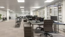Modern office space with contemporary furnishings, white walls, large windows, beige carpeting, and various office equipment