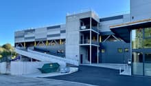 A multi-story commercial building with a gray and blue exterior. The building has a large garage door and a dumpster in the foreground, indicating it is likely a storage or warehouse facility.