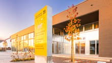Modern commercial building, yellow signboard, glass facade, entrance with automatic sliding doors, glass wall, tree in front, brick walkway, paved entrance area