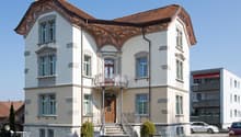 white house, brown roof, multiple windows, large entrance with steps, balcony