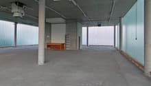 Empty concrete room, concrete flooring, large glass windows, small wooden desk.