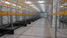 Rows of pallet racking system, numbered shelves, yellow and silver construction, fluorescent ceiling lights, clean and spacious with yellow lines on the floor