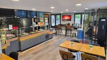 A modern restaurant with a wooden counter, black chairs, wooden tables, a fireplace, and a glass display case.
