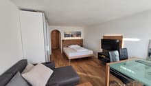 A room with a bed, couch, TV, dining table, and chairs.