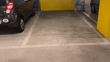 Underground parking with two available parking spaces labeled D21, concrete flooring, a yellow and white wall, a trash can near the wall, and cars parked inside.