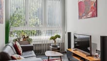 modern decor, brown sofa, coffee table, wall-mounted TV, wooden TV stand, floor lamps, decorative items, large window with vertical blinds